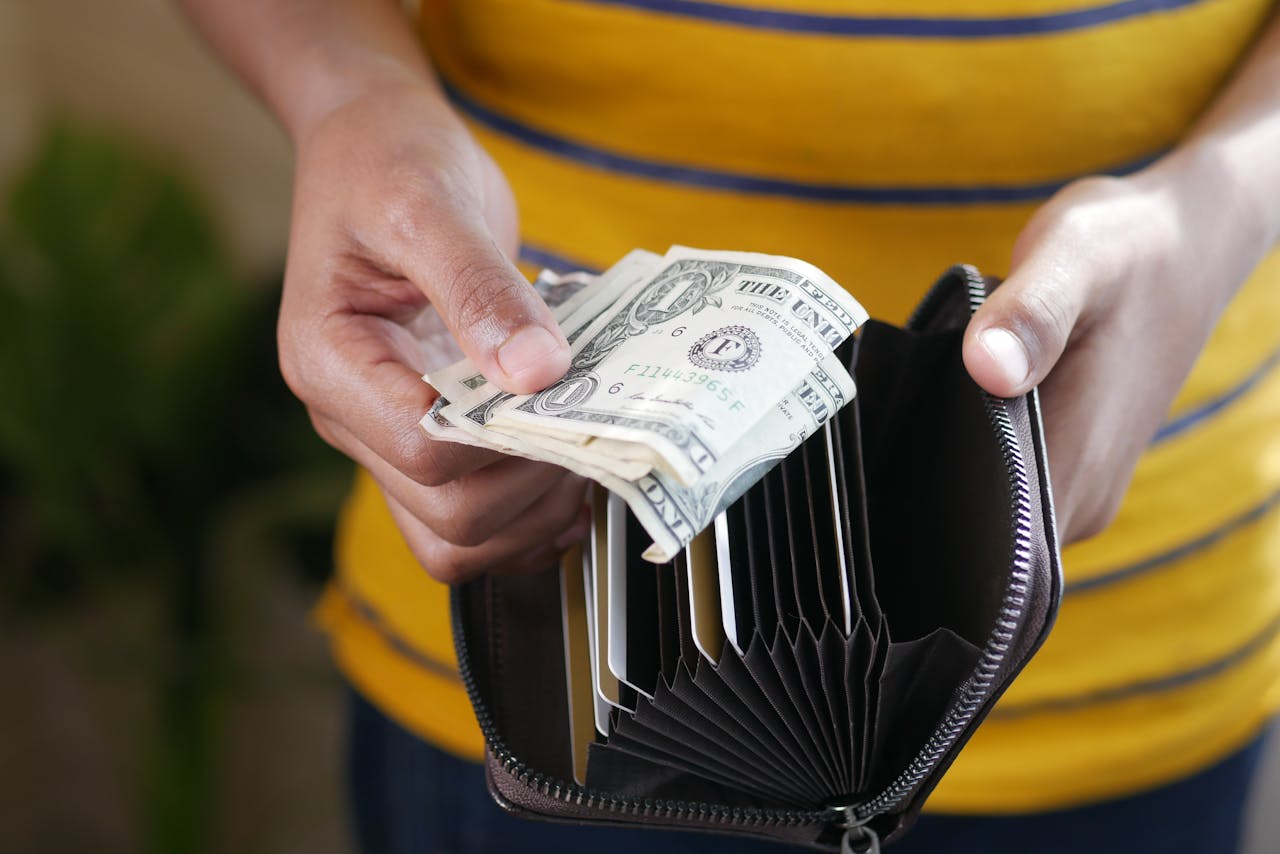 Close-up of a persons hands holding US dollar bills and a wallet.